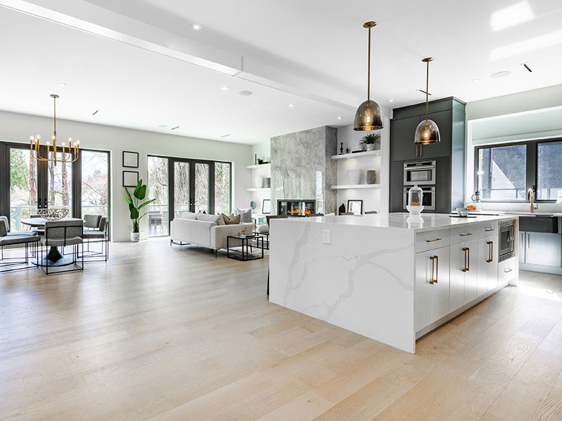 Open floor plan kitchen and living room in a modern luxury home with light wood floors and white walls.