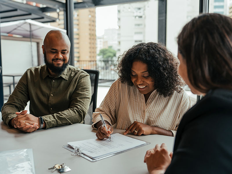 A couple signing home offer documents with a female realtor sitting at the table with them.