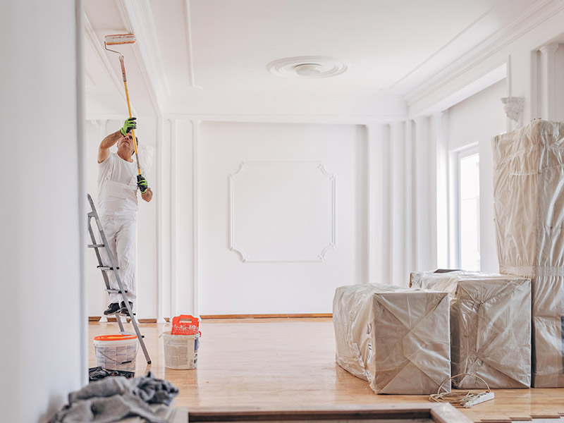 Male professional painting the ceiling of a modern room in white.